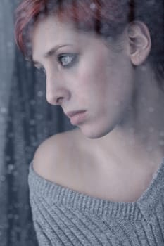 Young beautiful woman behind a rainy window on a dull rainy day