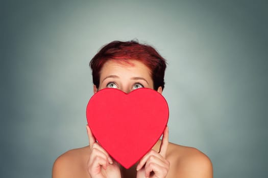 Young red-haired woman behind a red heart looks up