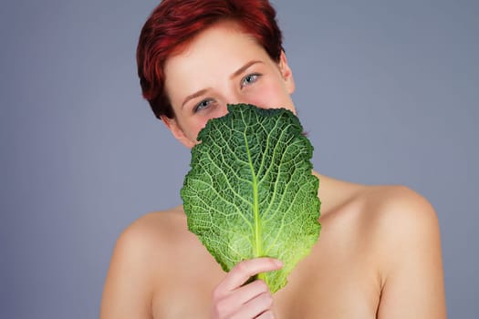 Young happy red-haired woman holds a leaf of savoy cabbage in front of her face