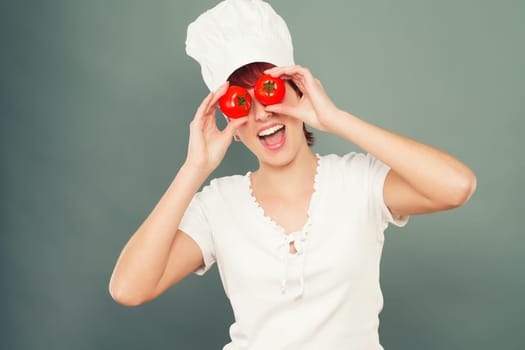 Young enthusiastic woman with chef's hat holds tomatoes in front of her eyes