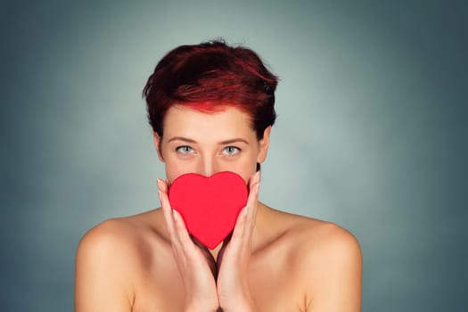 Young red-haired beautiful woman holds red heart in front of her face