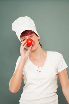 Young woman with chef's hat holds tomato in front of her nose