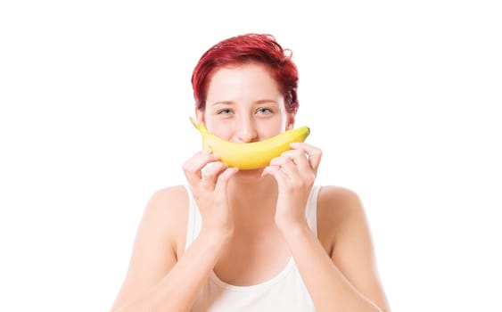 Young woman holds banana as a smile in front of her mouth against a white background