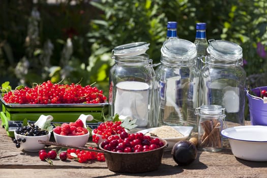 Ingredients for homemade fruit liqueur with fresh picked currants,raspberries and cherries on a wooden table