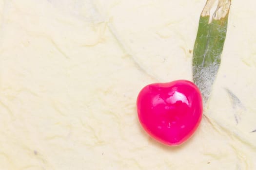 One heart candy in red color on light yellow mulberry paper background.