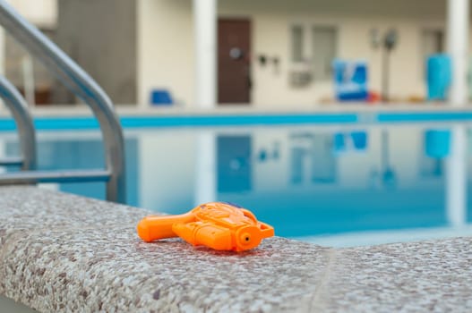 Colorful water pistol along edge of a swimming pool