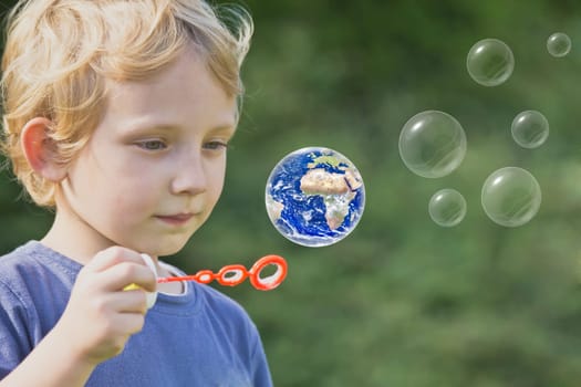 Caucasian blond boy is playing with soap bubbles. One of these bubbles is Earth globe.