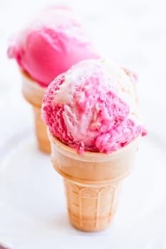 Closeup of two cones of raspberry and vanilla ice cream on light background