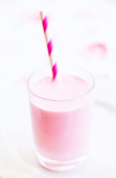 Closeup of raspberry smoothie made with milk and ice cream and with striped white and pink straw in glass on light background