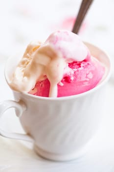 Closeup of cup with raspberry and vanilla ice cream and spoon on light background