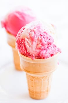 Closeup of two cones of raspberry and vanilla ice cream on light background