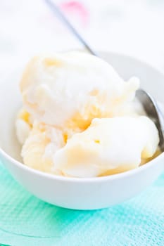 Closeup of scoops of vanilla ice cream and spoon in white bowl on light background