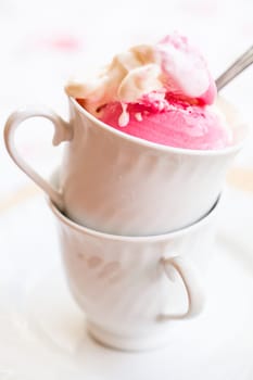 Closeup of cup with raspberry and vanilla ice cream and spoon on light background