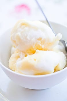 Closeup of scoops of vanilla ice cream and spoon in white bowl on light background