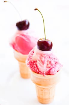 Closeup of two cones of raspberry and vanilla ice cream with cherry decorations on light background