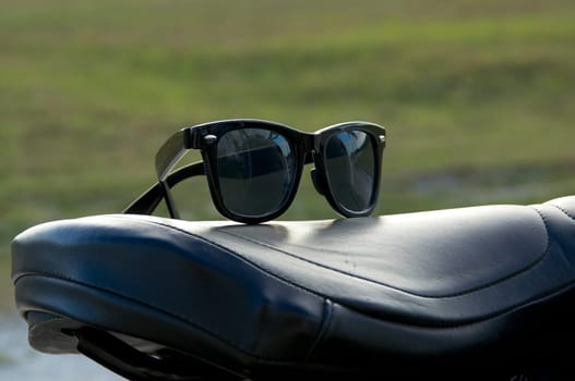 A pair of generic wayfarer sunglasses are on top of leather motorcycle seat. NOTE