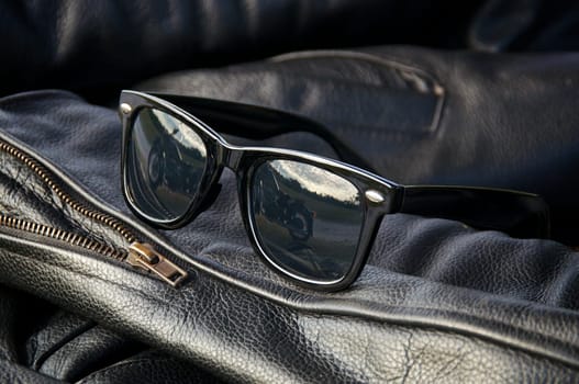 close up generic wayfarer sunglasses on sleeve of buffalo hide motorcycle jacket showing motorcycle in reflection. NOTE