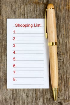 Pen and shopping list on wooden background