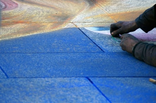The photograph of a man drawing a picture with chalk in a square.