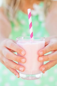 Closeup of glass of smoothie drink with straw held in hands by young girl