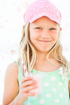 Smiling young girl holding milk fruit smoothie in glass with striped straw