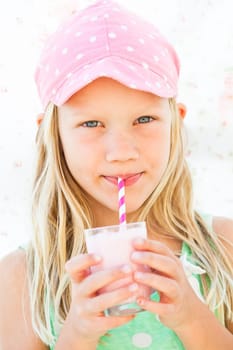 Cute young girl drinking milk fruit smoothie with striped straw from glass held in hands