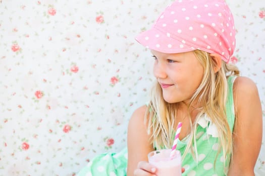 Smiling young girl holding milk fruit smoothie in glass with striped straw