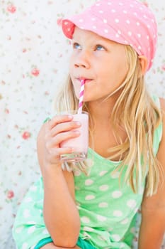 Cute young girl drinking milk fruit smoothie with striped straw from glass held in hand
