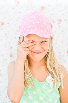 Portrait of cute smiling young girl looking through one eye while covering other eye with fingers