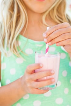 Closeup of glass of smoothie drink with straw held in hand by young girl