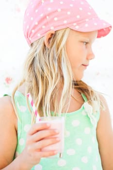 Serious looking cute young girl holding milk fruit smoothie in glass with striped straw