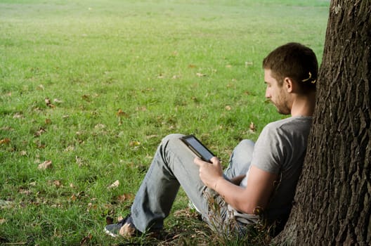 Young man reading e-book under the tree