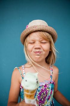 Cute young girl with funny expression holding ice cream cone outside against blue wall background