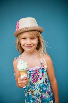 Cute smiling young girl holding ice cream cone outside against blue wall background