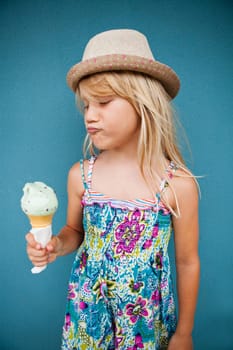 Cute young girl with funny expression holding ice cream cone outside against blue wall background