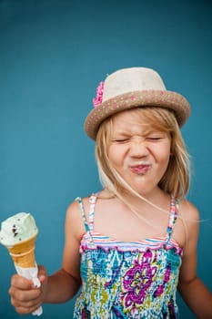 Cute young girl with funny expression holding ice cream cone outside against blue wall background