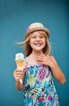 Cute smiling young girl holding ice cream cone outside against blue wall background