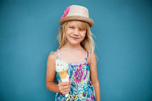 Cute smiling young girl holding ice cream cone outside against blue wall background