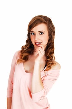 A beautiful young woman in a pink top and long curly hair standing for.white background with her hand on her chin..