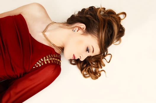 A young pretty woman in a red dress lying whit her long curly hair for.light beige background..