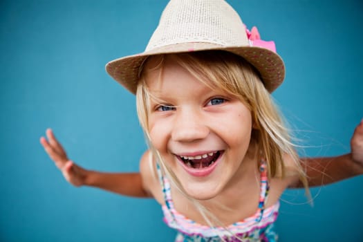 Portrait of stylish cute young girl being playful outside against blue wall background with focus on face