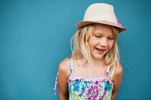 Portrait of stylish cute young girl smiling outside against blue wall background