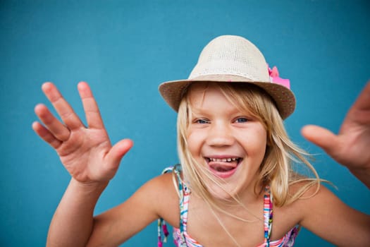 Portrait of stylish cute young girl being playful outside against blue wall background