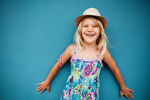 Portrait of stylish cute young girl smiling outside against blue wall background