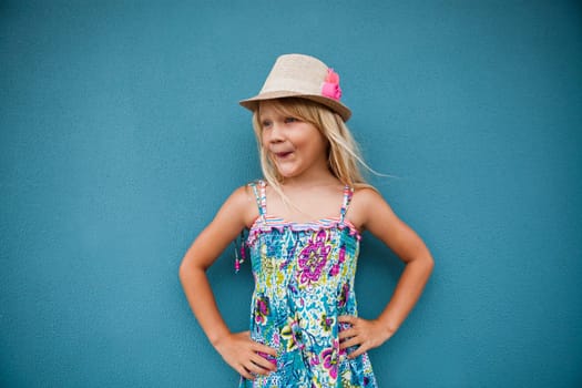 Portrait of stylish cute young girl with funny expression outside against blue wall background