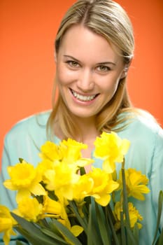 Smiling woman holding yellow narcissus spring flowers on orange background