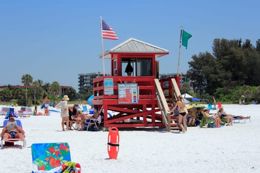 SIESTA KEY, FLORIDA - MAY 9, 2013: Red lifeguard tower flying green and American flags with a lifeguard present and lots of people around relaxing at  beautiful Siesta Beach on a very sunny, warm day