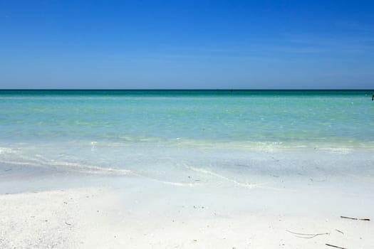 Beautiful distant view of calm, clear Gulf coast turquoise tropical water and horizon seen from the white quartz sand shore of Siesta Beach under a sunny blue sky.