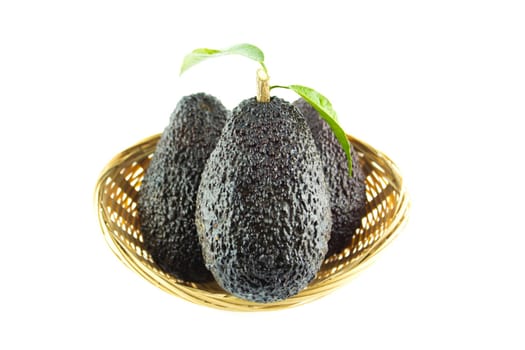 Avocados with leaves on a Dish of straw.