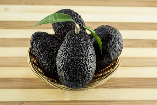 Avocados with leaves on a Dish of straw.